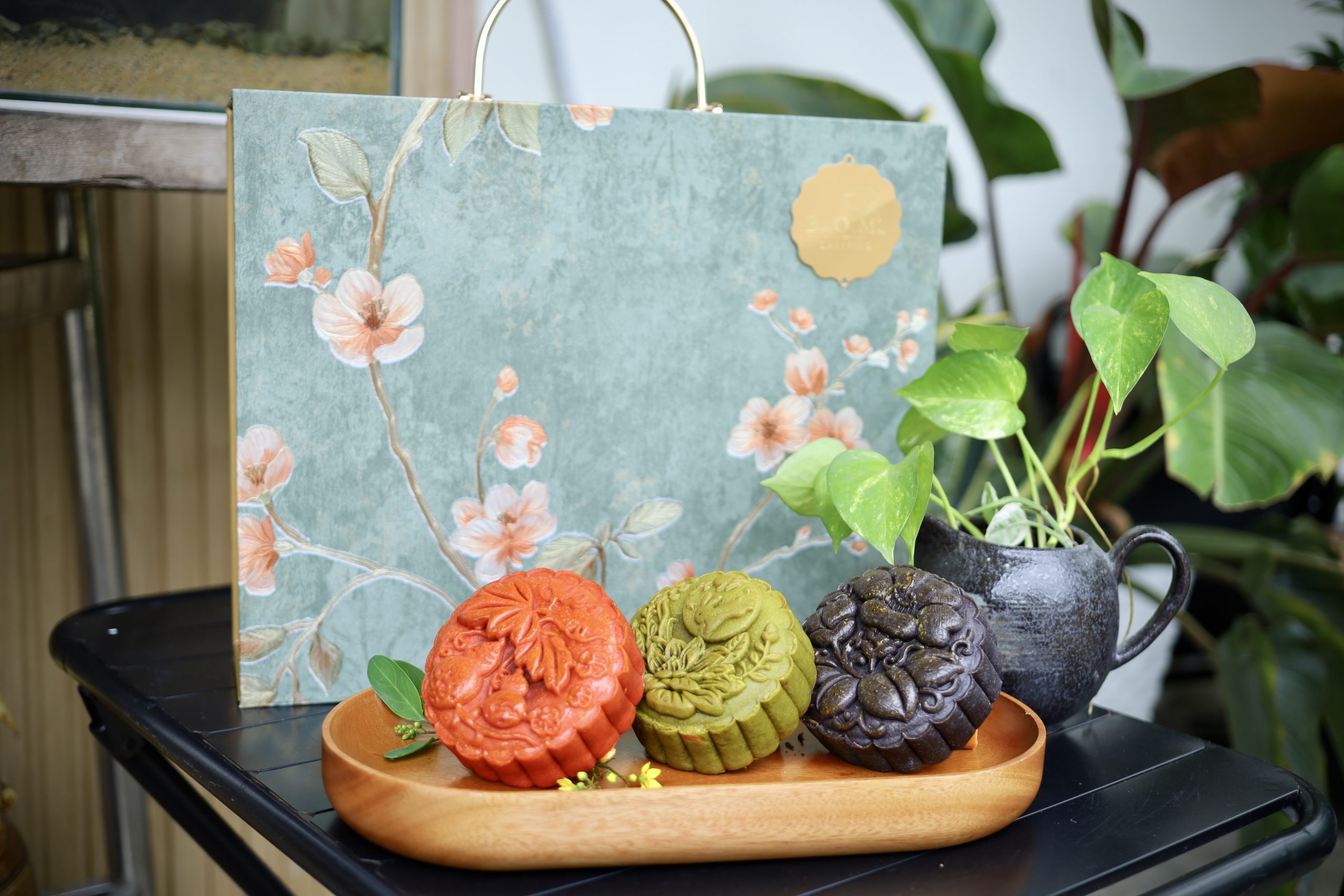 Hộp bánh trung thu Nguyệt Chi Giao Hảo sang trọng với ba chiếc bánh màu đỏ, xanh và đen, thiết kế tinh tế từ B.O.M Catering